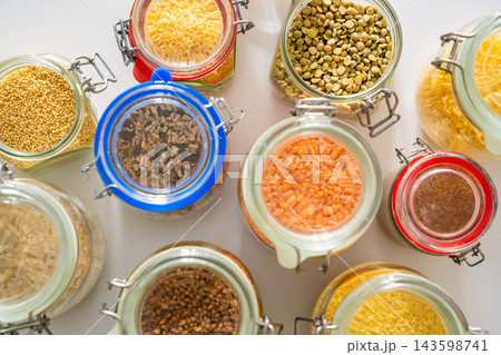 Tow view of assorted grains, legumes and seeds stored in glass jars with clasp lids on a kitchen counter. Organized pantry storage supports meal planning and a low waste household lifestyle Tow view of assorted grains, legumes and seeds stored in glass jars with clasp lids on a kitchen counter. Organized pantry storage supports meal planning and a low waste household lifestyle 143598741