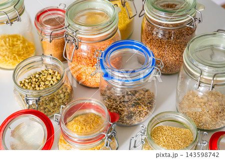 Assorted grains, legumes and seeds stored in glass jars with clasp lids on a kitchen counter. Organized pantry storage supports meal planning and a low waste household lifestyle 143598742