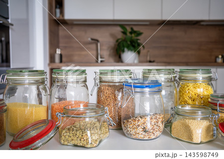 Glass jars filled with assorted grains, lentils and seeds arranged on a modern kitchen countertop. Organized pantry storage promotes sustainable housekeeping and a clutter free home 143598749