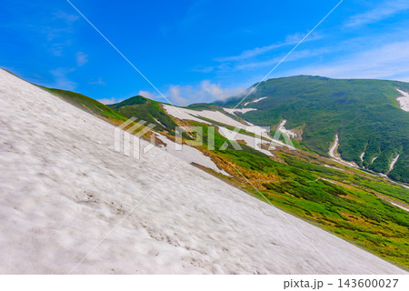 夏の月山登山で残雪の雪原の斜面越しに快晴の青空のもとそびえる月山山頂方向の山並みを捉えた夏山風景 夏の月山登山で残雪の雪原の斜面越しに快晴の青空のもとそびえる月山山頂方向の山並みを捉えた夏山風景 143600027