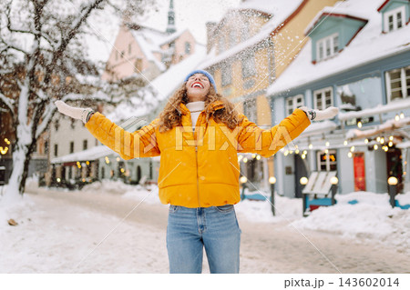 Smiling woman in a bright jacket is having fun with the snow on a snowy city street. Smiling woman in a bright jacket is having fun with the snow on a snowy city street. 143602014