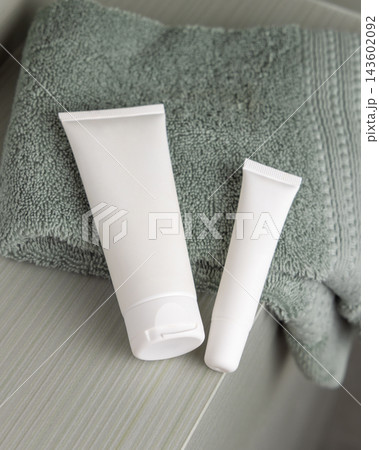 White cream tubes mockup near green terry towel in bathroom closeup, unbranded cosmetic packaging White cream tubes mockup near green terry towel in bathroom closeup, unbranded cosmetic packaging 143602092