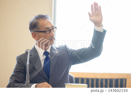 法廷で着席したまま手を挙げるベテラン男性検事 法廷で着席したまま手を挙げるベテラン男性検事 143602150