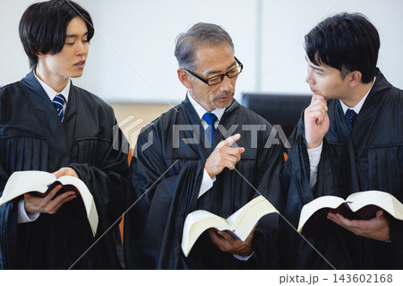法律書を見ながら話し合うベテランと若手の裁判官3人 143602168