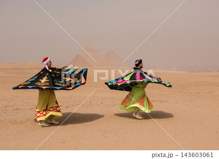 Two Egyptian sufi whirling dervish performers spinning vibrant colorful robes at the Great Pyramids of Giza in Egypt ideal for travel tourism and MENA Two Egyptian sufi whirling dervish performers spinning vibrant colorful robes at the Great Pyramids of Giza in Egypt ideal for travel tourism and MENA 143603061