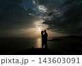 Couple embracing passionately by seaside at sunset with dramatic clouds and warm light 143603091