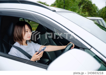 車の運転席でスマホを見る若い女性 車の運転席でスマホを見る若い女性 143603218