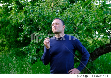 Middle aged country man holding grass stem in teeth and standing thoughtfully near apple tree in rural garden Middle aged country man holding grass stem in teeth and standing thoughtfully near apple tree in rural garden 143603451