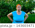 Senior red haired woman standing with hands on hips looking tired sad and disappointed beneath apple tree in summer garden 143603471