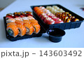 Soy sauce in plastic container near black sushi takeaway boxes delivery food close up dining scene on table  143603492