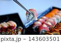 Sushi delivery set with tuna rolls in black containers, chopsticks dipping into soy sauce during takeaway meal presentation 143603501