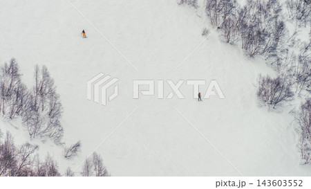 Two skiers descending wide snowy mountain slope framed by leafless birch trees in winter landscape Two skiers descending wide snowy mountain slope framed by leafless birch trees in winter landscape 143603552