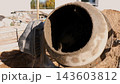 Mud covered concrete mixer drum at construction site, shown close up beside piles of soil and unfinished building materials in bright daylight, highlighting heavy work and building progress. 143603812