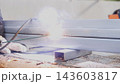 Close up of gloved worker welding metal beams with intense sparks and smoke during outdoor repair work, showing industrial fabrication, construction maintenance, steel surfaces, and bright sunlight 143603817