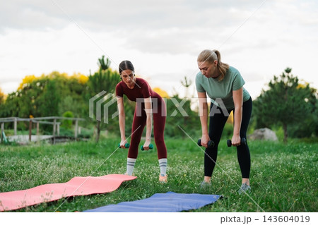 Women exercising in a park while lifting weights during sunset hours 143604019