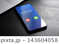 Unknown caller warning displayed on smartphone with suspected spam notification near laptop. Phone fraud prevention, robocall blocking and mobile protection concept 143604058