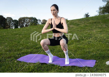 Sunny outdoor workout featuring a woman practicing squats on a yoga mat 143604075