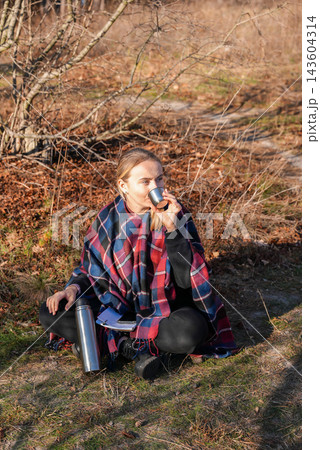 Young woman pouring hot drink from thermos during outdoor break Young woman pouring hot drink from thermos during outdoor break 143604314
