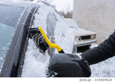 Man Brushing Snow Off Car During Winter. Seasonal outdoor activity shows vehicle maintenance snow removal and preparation for driving in cold conditions Man Brushing Snow Off Car During Winter. Seasonal outdoor activity shows vehicle maintenance snow removal and preparation for driving in cold conditions 143604620