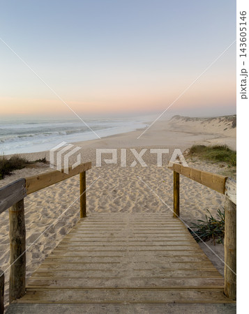 Wooden walkway leading down to a serene sandy beach in Furadouro under a soft, misty twilight sky 143605146