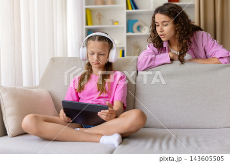 Mother watching her daughter using tablet with headphones while sitting at home 143605505