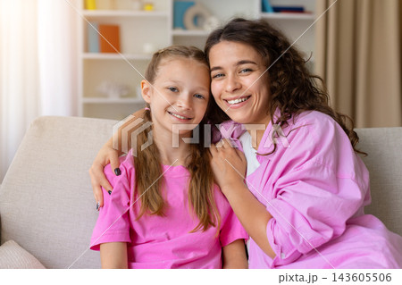 Smiling mother embracing her daughter while posing together on sofa at home 143605506