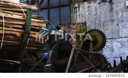 Lumber stacked at an old sawmill, industrial machinery, and a concrete wall showing timber processing industry 143605932