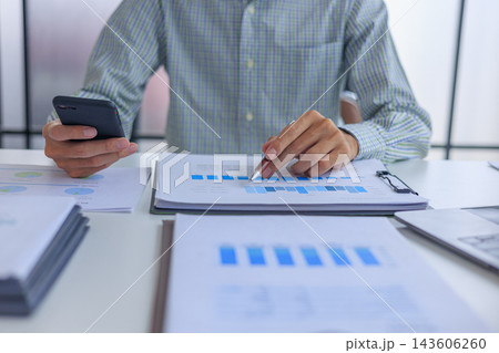 Professional financial analyst working on analyzing charts and documents using smartphone in modern office. 143606260