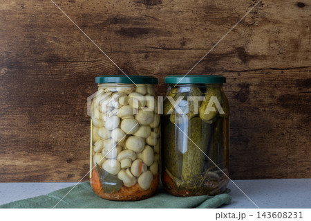 Pickled mushrooms and cucumbers in jars for winter storage on rustic wooden background Pickled mushrooms and cucumbers in jars for winter storage on rustic wooden background 143608231