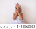 Blonde Girl Wearing Princess Crown and Dress Covering Mouth with Hands  143608392