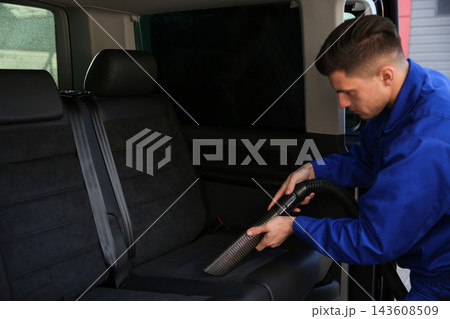 Car wash worker vacuuming upholstery on automobile seat 143608509