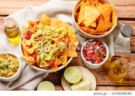 Mexican nachos tortilla chips in a ceramic bowl, topped with guacamole, chopped tomatoes, and green olives. 143608646