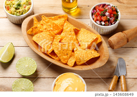 Crispy corn tortilla nachos served with guacamole, fresh tomato salsa, and creamy cheddar cheese on a wooden table. 143608649