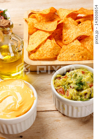 Golden, crispy tortilla chips served on a square wooden tray with creamy cheddar cheese sauce, set on a rustic wooden table. Mexican cuisine Golden, crispy tortilla chips served on a square wooden tray with creamy cheddar cheese sauce, set on a rustic wooden table. Mexican cuisine 143608654