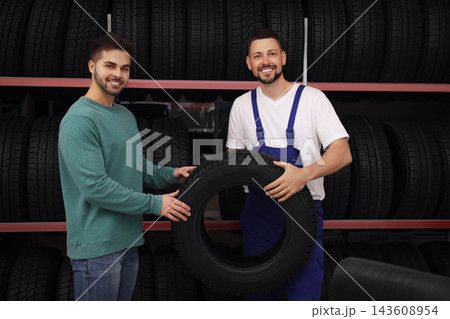 Mechanic helping client to choose car tire in auto store Mechanic helping client to choose car tire in auto store 143608954