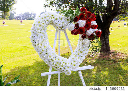 Large heart-shaped flower arrangement stands on an easel at memorial service in park on cemetery setting Large heart-shaped flower arrangement stands on an easel at memorial service in park on cemetery setting 143609483