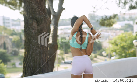 Woman Stretches Triceps Outdoors With Trees Beyond 143609529