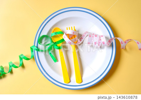 A measuring tape and fork on white plate on background. A measuring tape and fork on white plate on background. 143610878