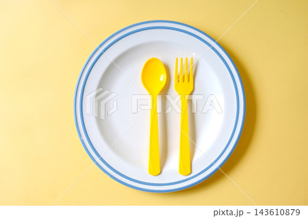 Yellow spoon and fork on white plate over color background. 143610879