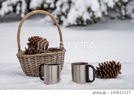 Two metal camping mugs and pine cones in winter snow 143611117