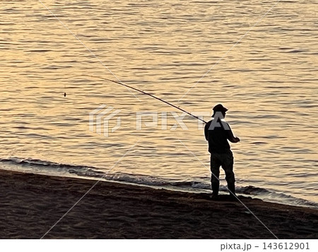 夕日に輝く海辺で釣りをする釣り人のシルエット 143612901