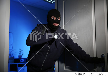 Thief with flashlight breaking into house at night 143613270