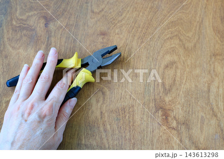Hand holding pliers against a wooden background with space for text. Start of a repair project, artisan, DIY and manual craft Hand holding pliers against a wooden background with space for text. Start of a repair project, artisan, DIY and manual craft 143613298