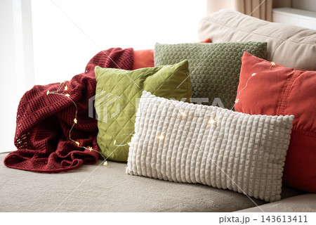 Cozy living room sofa decorated with colorful pillows and glowing fairy lights 143613411