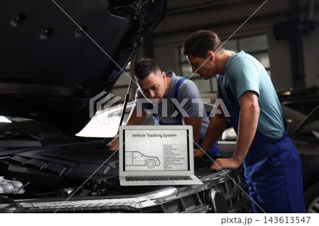 Laptop with vehicle tracking system and blurred mechanics on background. Auto diagnostic 143613547