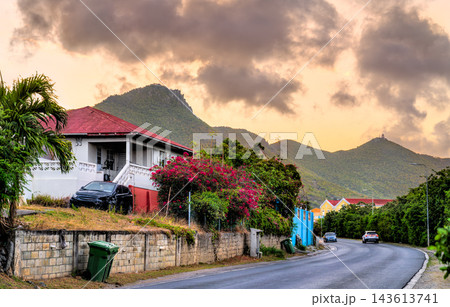 A residential house at Bush Road with tropical foliage and mountain peaks under a sunset sky in Philipsburg, Sint Maarten, Caribbean Netherlands A residential house at Bush Road with tropical foliage and mountain peaks under a sunset sky in Philipsburg, Sint Maarten, Caribbean Netherlands 143613741
