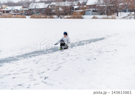 Child sliding on frozen pond in winter village Child sliding on frozen pond in winter village 143613861