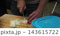 Woman Slicing White Onion on Wooden Cutting Board 143615722
