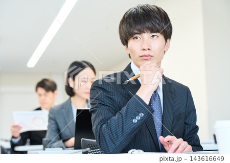 オフィスで資料を見ながらチームで仕事をする若い会社員 143616649
