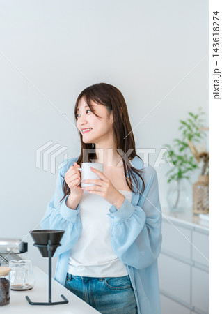 明るい家のキッチンでコーヒーカップを持って微笑む若い女性。穏やかな暮らしとリラックスタイム 143618274